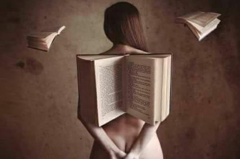 Una mujer desnuda de espalda con un libro delante