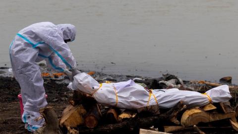 Un hombre junto al cadáver de un fallecido por covid-19 antes de su cremación a orillas del río Ganges, en Garhmukteshwar (Uttar Pradesh, la India), el 6 de mayo de 2021.